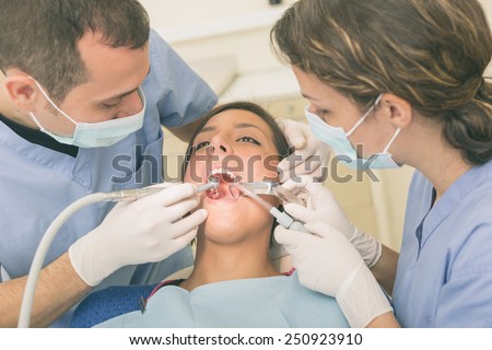 Dentist and Dental Assistant examining Patient teeth. Dentist is a Man, Assistant and Patient are Women. Patient is Relaxed and not scared of Dentist.