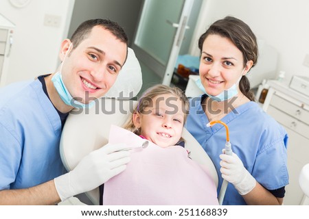 Dentist and Dental Assistant Portrait with Young Patient. Dentist is a Male, Assistant and Patient are Females. All the People are looking at camera with Smiling Expressions.