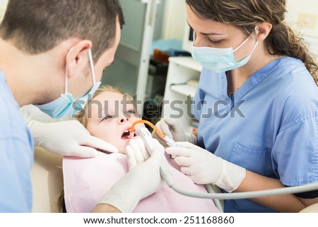 Dentist and Dental Assistant examining Young Girl teeth. Dentist is a Male, Assistant and Patient are Females. Patient is a Young Girl, she\'s Smiling and not scared of Dentist.