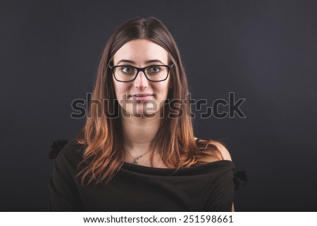Young Woman Portrait on Black Background. She has a Piercing inside the Mouth on Upper Lip. She also Wears Glasses. Head and Shoulders shot.