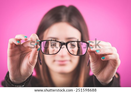 Young Woman with Eyesight Problems on Fuchsia Background. She Looks through her Glasses and holds them with both hands. Head and Shoulders shot.