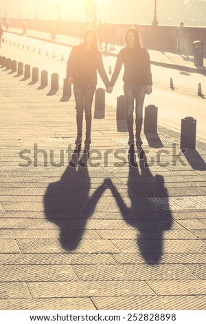 Shadows of Female Twins Holding Hands in the City. The Shadow is the Main Subject of the Photo. Girls are standing and Holding Hands. Backlight Shot. Focus on Shadow.