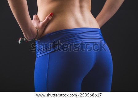 Sporty Female Bum and Back on Black Background. She is standing with Hands on Hips, Wearing Leggings and Top. Close Up shot.