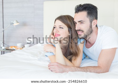 Young couple embraced on the bed. They are in a modern hotel room and they wear underwear. They embrace each other and look out of window. Love and lifestyle concepts.