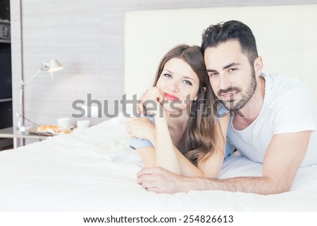 Young couple embraced on the bed. They are in a modern hotel room and they wear underwear. They embrace each other and look at camera. Love and lifestyle concepts.