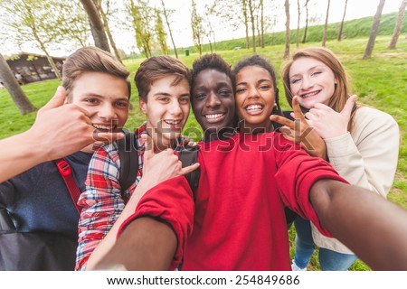 Group of multiethnic teenagers taking a selfie at park. Two boys and one girl are caucasian, one boy and one girl are black. Friendship, immigration, integration and multicultural concepts.