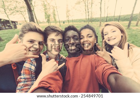 Group of multiethnic teenagers taking a selfie at park. Two boys and one girl are caucasian, one boy and one girl are black. Friendship, immigration, integration and multicultural concepts.
