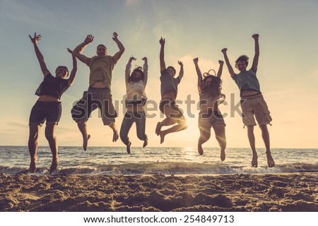 Multiracial group of people jumping at beach. Backlight shot. Happiness, success, friendship and community concepts.