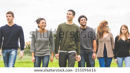 Multiethnic group of friends at park walking and enjoying time all together. Mixed race group with caucasian, black and asian people. Friendship, lifestyle, immigration concepts.