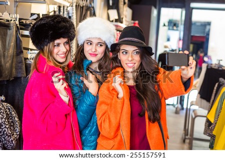 Three women taking a selfie wearing colorful coats in a clothing store. They are happy and enjoy funny clothes. Shopping concept, also related to social media addiction.