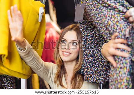 Beautiful girl at clothes shop looking for a dress, rooting around through the shelves. Behind the shelf view. Shopping concept.