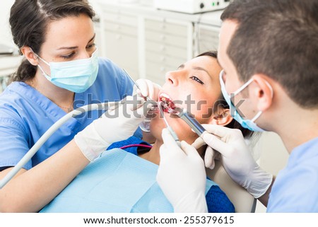Dentist and dental assistant examining patient teeth. Dentist and Patient are Women, Assistant is a Man. Patient is Relaxed and not scared of Dentist.