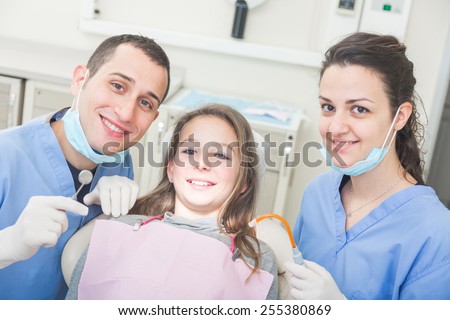 Dentist and dental assistant portrait with young patient. Dentist is a male, assistant and patient are females. All the people are looking at camera with Smiling expressions.