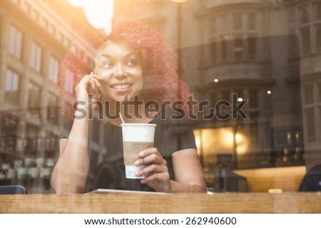 Beautiful girl with curly red hair talking on smart phone in a cafe, seen through the window with buildings reflections