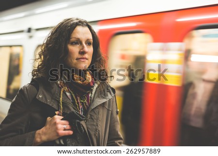 Beautiful woman at tube station in London with blurred train passing on background. She wears winter clothes and look in front of her while waiting for the train.