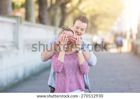 Young man making a surprise to a girl, covering her eyes from back and laughing.