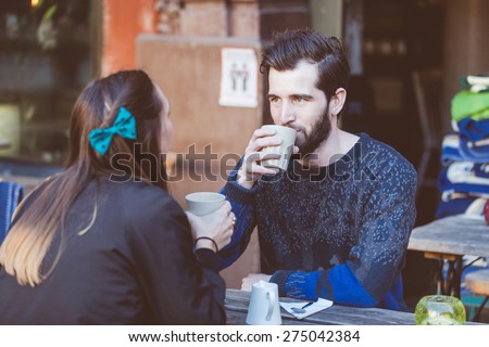 Hipster couple drinking coffee in Stockholm old town. They\'re sitting face to face. The man is wearing a blue sweater and the woman a striped shirt with black leather jacket.