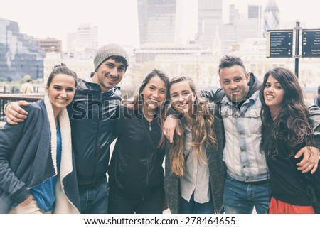 Group of friends embraced together in London. They are four girls and two boys in their twenties, friendship and lifestyle concepts, autumn clothing