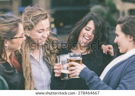 Group of women enjoying a beer at pub in London. They are embraced and laughing. Outdoor scene, winter season, friendship concept.