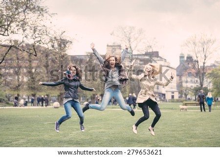 Group of women jumping at park in Copenhagen. They are in their twenties and they are wearing smart casual clothes. Happiness, friendship and success concepts.