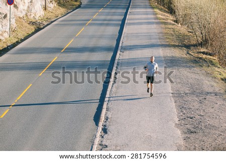 Young man running outside along an empty mountain road in the early morning. He has nordic features, and he\'s wearing black shorts and a gray sweater.