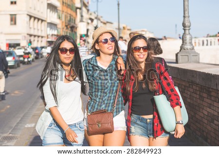 Three happy women walking in the city, talking each other and smiling. This is a mixed race group, one girl is half asian and one is middle eastern. Lifestyle, friendship and urban life concepts.