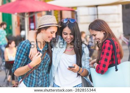Three young women with smart phone in the city, talking and smiling. This is a mixed race group, one girl is half asian and one is middle eastern. Lifestyle, friendship and urban life concepts.