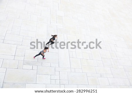Two women running in the city, aerial view. They are wearing gray and black sportswear.