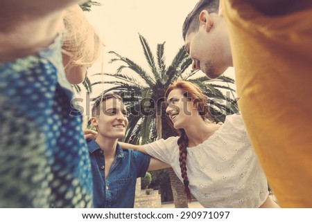 Group of teenagers embraced in circle, bottom view. They are two girls and two boys, smiling and looking down to the camera.