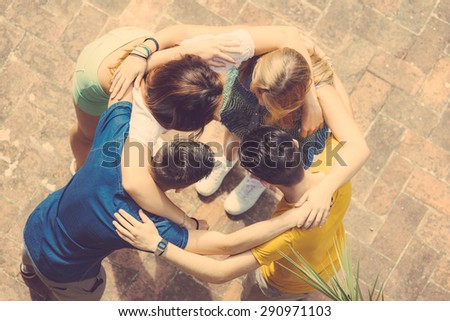 Group of teenagers embraced in circle, aerial view. They are two girls and two boys, looking each other
