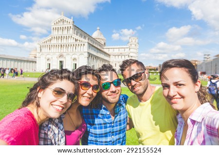 Group of tourists or friends taking a selfie in Pisa, Italy, with famous leaning tower on background. They are two men and three women. Lifestyle, friendship and travel concepts.