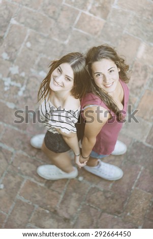 Portrait of two beautiful girls taken from above. They are standing back to back and looking up at camera. Lifestyle and friendship concepts. Vintage filter applied.