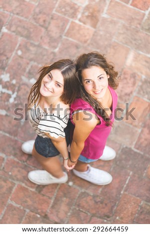 Portrait of two beautiful girls taken from above. They are standing back to back and looking up at camera. Lifestyle and friendship concepts.
