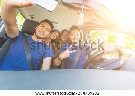 Group of friends taking a selfie into the car before leaving for vacations. They are a mixed race group of four persons, two caucasian and two hispanic.