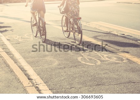 Couple of female friends riding bikes on the street. Focus on bike icon. They are two women wearing summer clothes are riding bikes. They are on the cycle track along a city road.