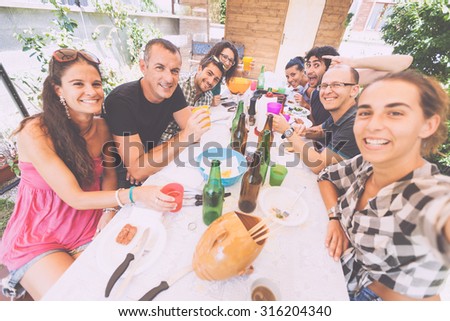 Group of people taking selfie while having lunch outdoor. A multicultural group of friends is taking a selfie while eating. They are happy and there are a lot of plates and bottles on the table.