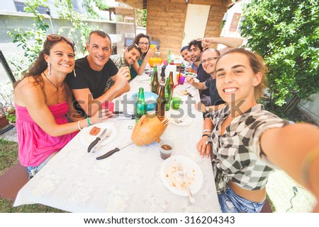 Group of people taking selfie while having lunch outdoor. A multicultural group of friends is taking a selfie while eating. They are happy and there are a lot of plates and bottles on the table.