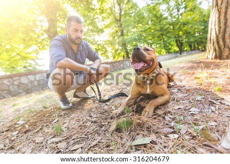 Man with his dog at park. He is looking at his dog standing with open mouth. The main subject is the dog, the man is blurred on the background.