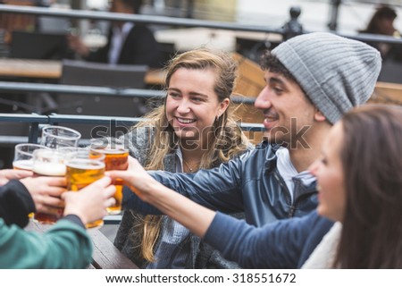 Group of friends enjoying a beer at pub in London, toasting and laughing. Close up on two girls and a boy.