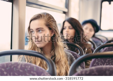 Portrait of a blonde woman on a bus, with other people on background. She has long blond hair and a candid smile. Transportation and travel theme.