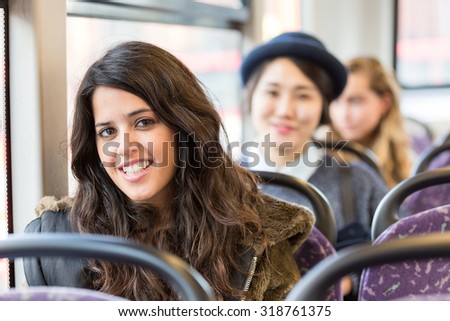 Portrait of a spanish woman on a bus, with other people on background. She has long black hair and a candid smile. Transportation and travel theme.