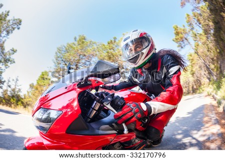 Woman driving a motorbike on a countryside road. Close up photo, the face of the woman is visible, there are some blurred trees on background. Transportation and speed concepts.