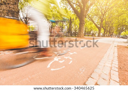 Blurred rider cycling on bike lane in Dusseldorf . Low angle view with cyclist going from left to right. Many trees on background. Sustainable commuting, transportation and lifestyle concepts.