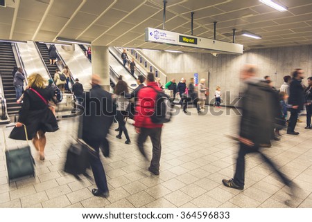 Blurred people walking inside train station or airport, with luggage and bags. There are some escalators on background, with people walking on both directions. Travel and urban lifestyle concepts.