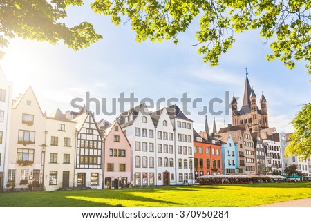 Houses and park in Cologne, Germany. Many of them are colourful, they are facing a public park with green grass and some trees. There is a bell tower on background. Travel and architecture concepts.