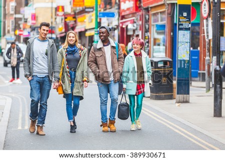 Group of young friends walking in famous Brick Lane in London. Multicultural people with mixed races wearing colourful clothes having fun together. They could be students or tourists