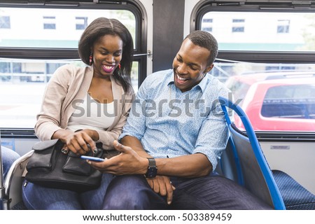 Happy black couple travelling by bus in Chicago. A man and a woman sitting in the bus and looking at the smartphone. They are laughing and enjoying time together. Lifestyle and happiness concepts.