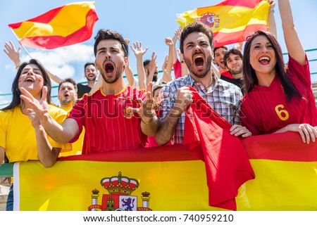Spanish supporters cheering at stadium with flags. Group of fans watching a match and cheering team Spain. Sport and lifestyle concepts.