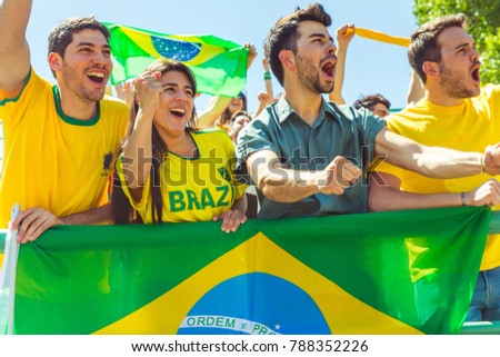 Brazilian supporters celebrating at stadium with flags. Group of fans watching a match and cheering team Brazil. Sport and lifestyle concepts.