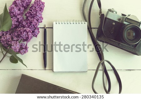 Old notebook tamplate, vintage film camera, lilac, vintage book, on white wooden background.